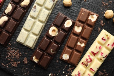 Photo of Different tasty chocolate bars with nuts and freeze dried raspberry on black table, flat lay