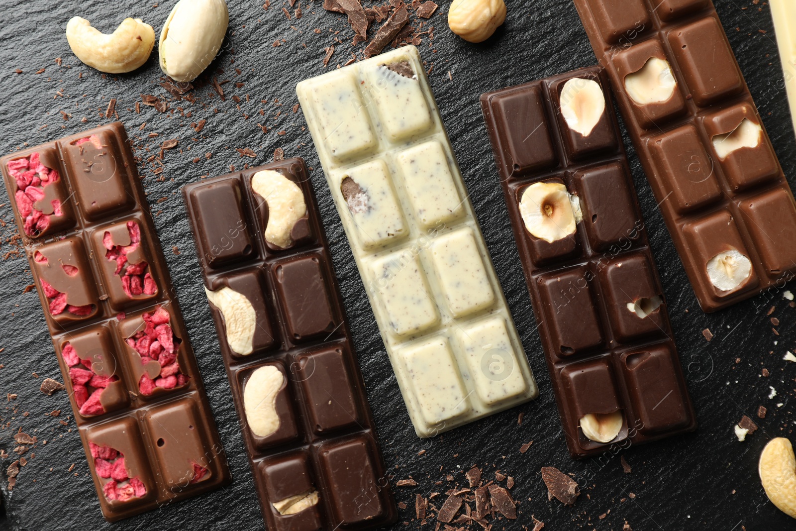 Photo of Different tasty chocolate bars with nuts and freeze dried raspberry on black table, flat lay