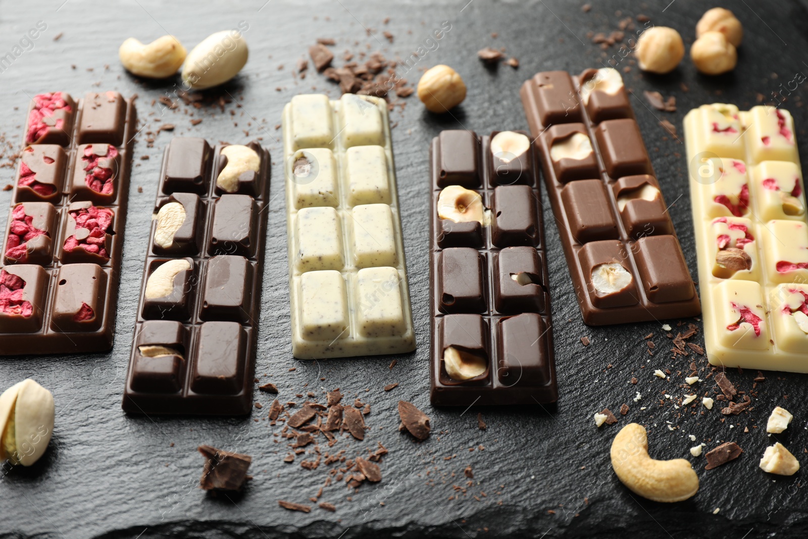 Photo of Different tasty chocolate bars with nuts and freeze dried raspberry on black table, above view