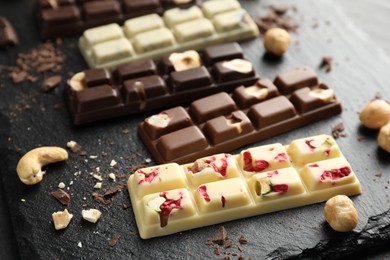 Photo of Different tasty chocolate bars with nuts and freeze dried raspberry on black table, closeup