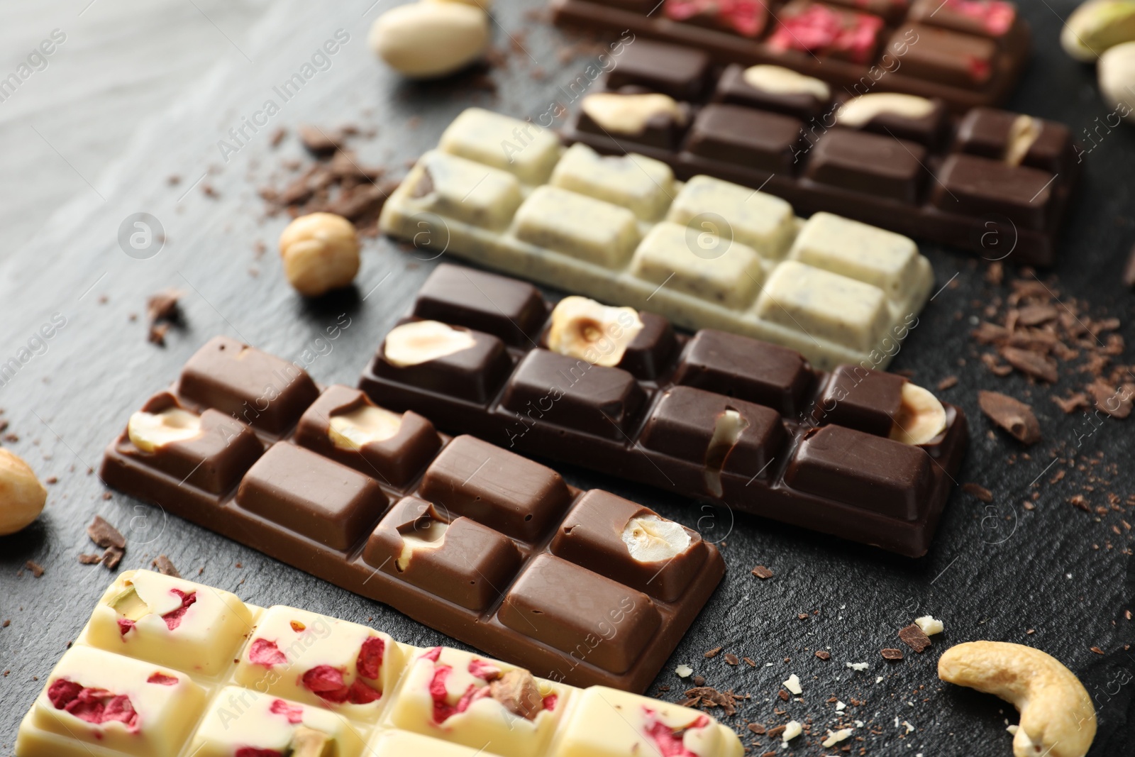 Photo of Different tasty chocolate bars with nuts and freeze dried raspberry on black table, closeup