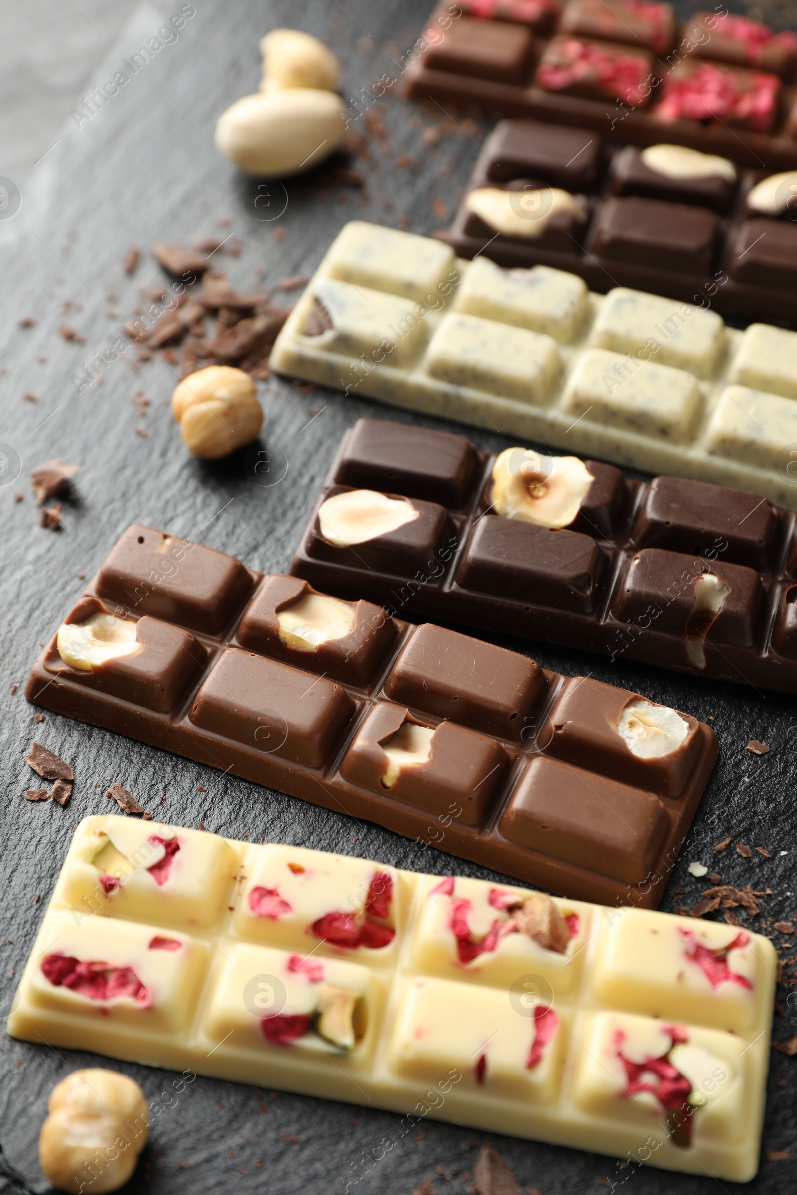 Photo of Different tasty chocolate bars with nuts and freeze dried raspberry on black table, closeup