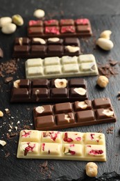 Photo of Different tasty chocolate bars with nuts and freeze dried raspberry on black table, closeup