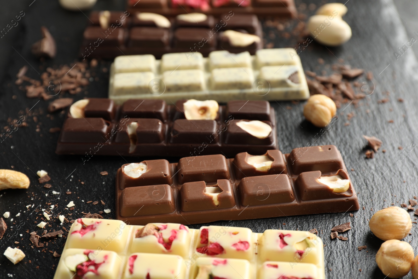 Photo of Different tasty chocolate bars with nuts and freeze dried raspberry on black table, closeup