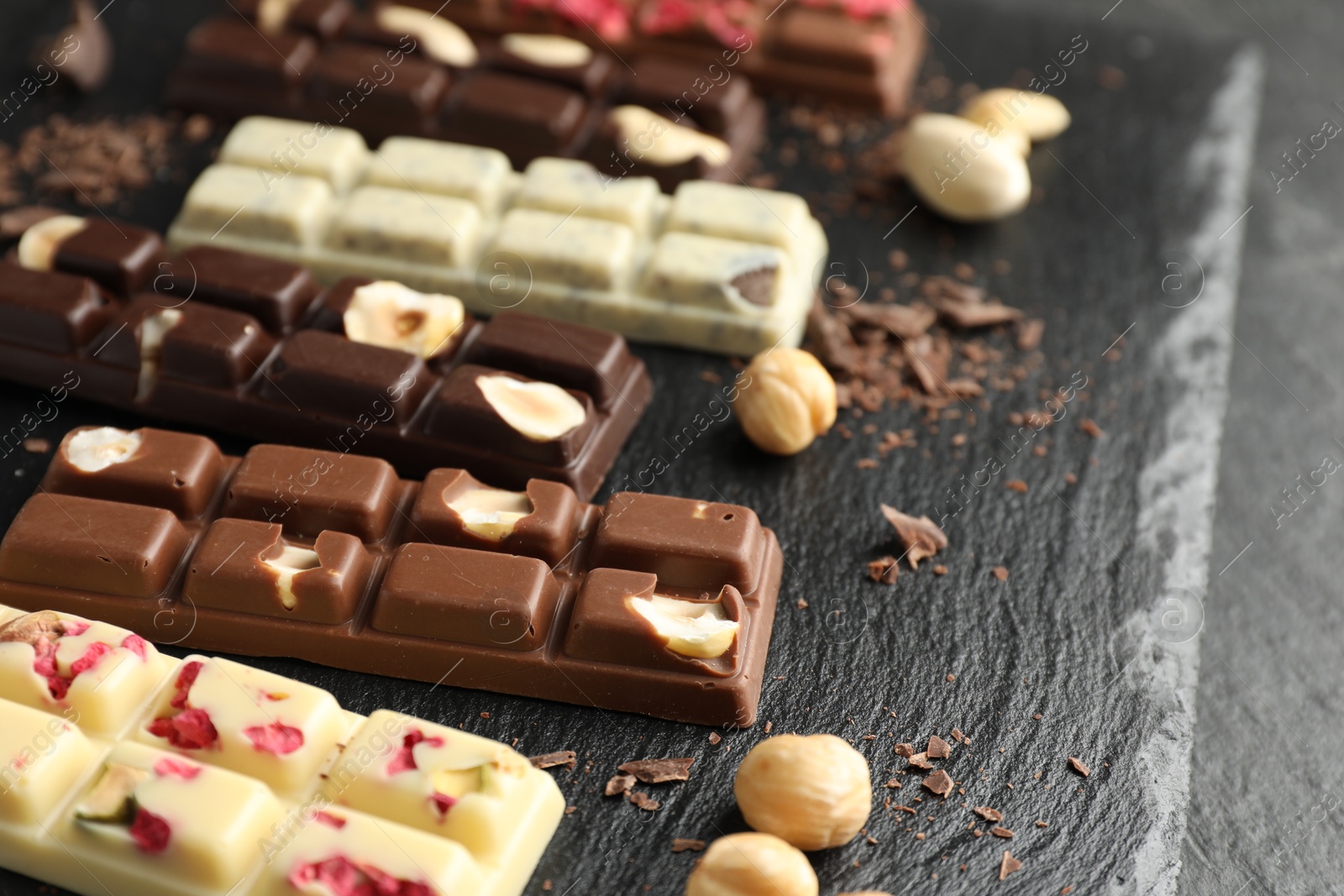 Photo of Different tasty chocolate bars with nuts and freeze dried raspberry on black table, closeup