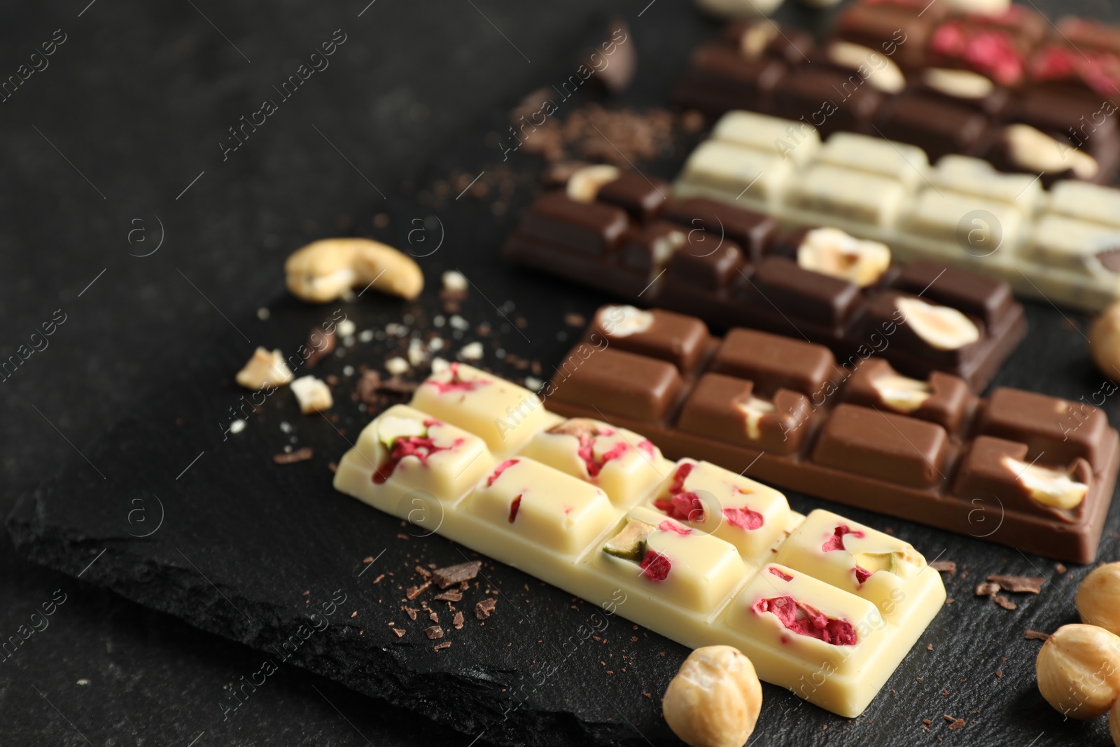 Photo of Different tasty chocolate bars with nuts and freeze dried raspberry on black table, closeup