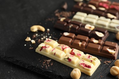 Photo of Different tasty chocolate bars with nuts and freeze dried raspberry on black table, closeup