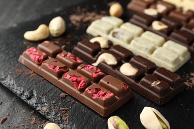 Photo of Different tasty chocolate bars with nuts and freeze dried raspberry on black table, closeup