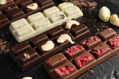 Photo of Different tasty chocolate bars with nuts and freeze dried raspberry on black table, closeup