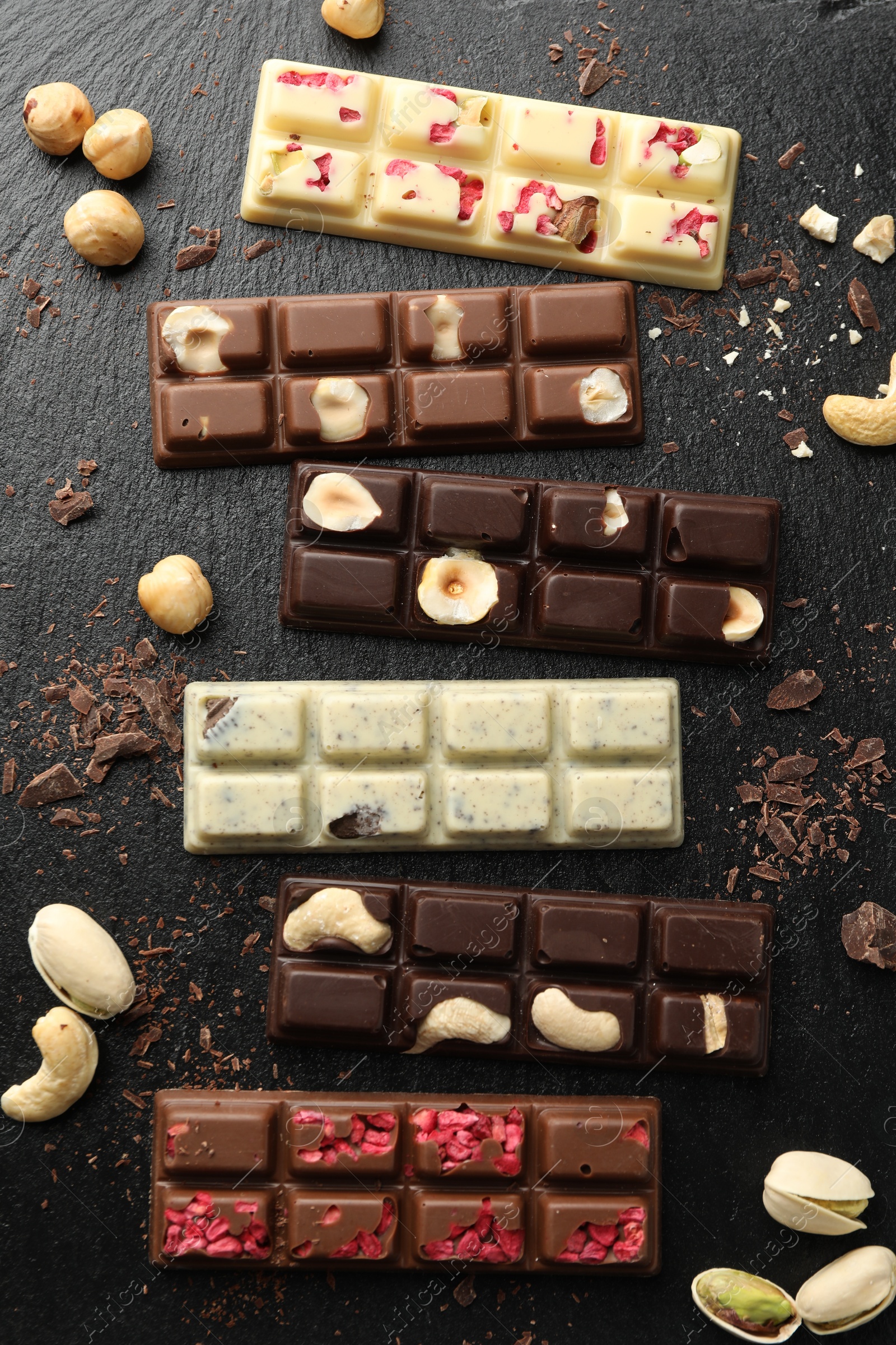 Photo of Different tasty chocolate bars with nuts and freeze dried raspberry on black table, flat lay