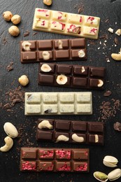 Photo of Different tasty chocolate bars with nuts and freeze dried raspberry on black table, flat lay