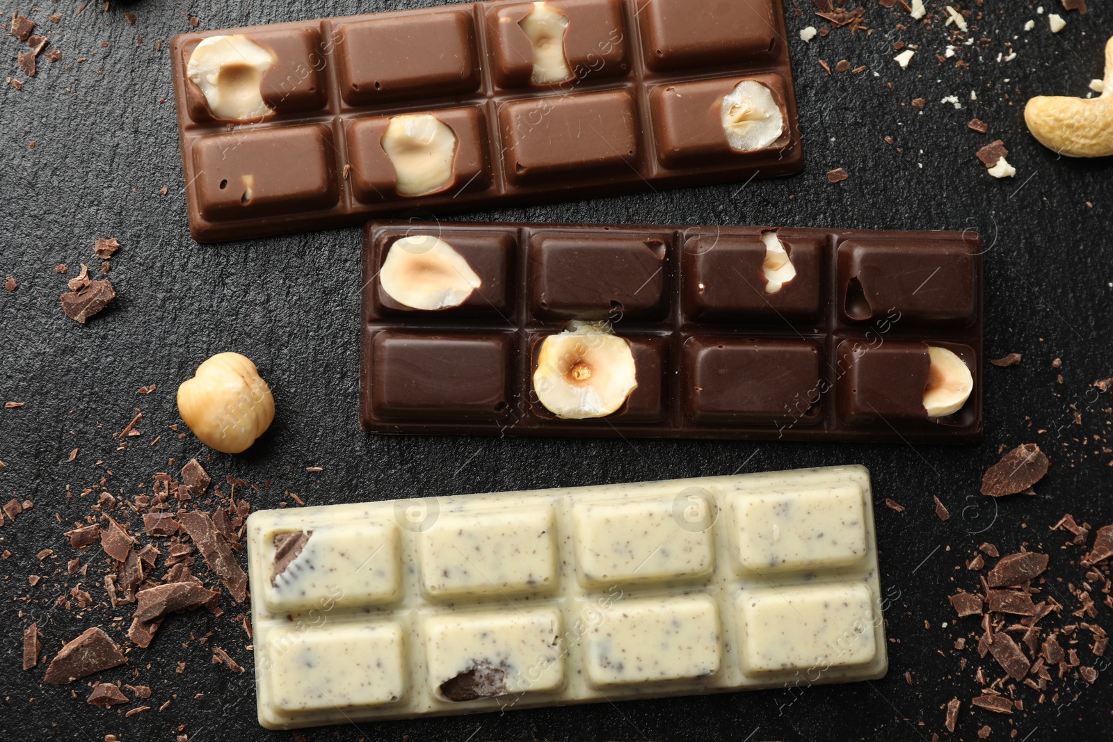 Photo of Different tasty chocolate bars with nuts on black table, flat lay