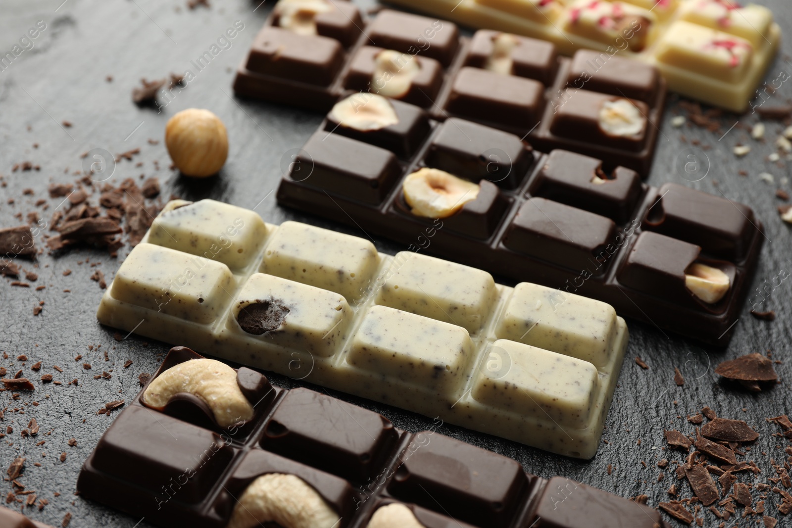 Photo of Different tasty chocolate bars with nuts on black table, closeup