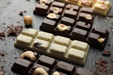 Photo of Different tasty chocolate bars with nuts on black table, closeup