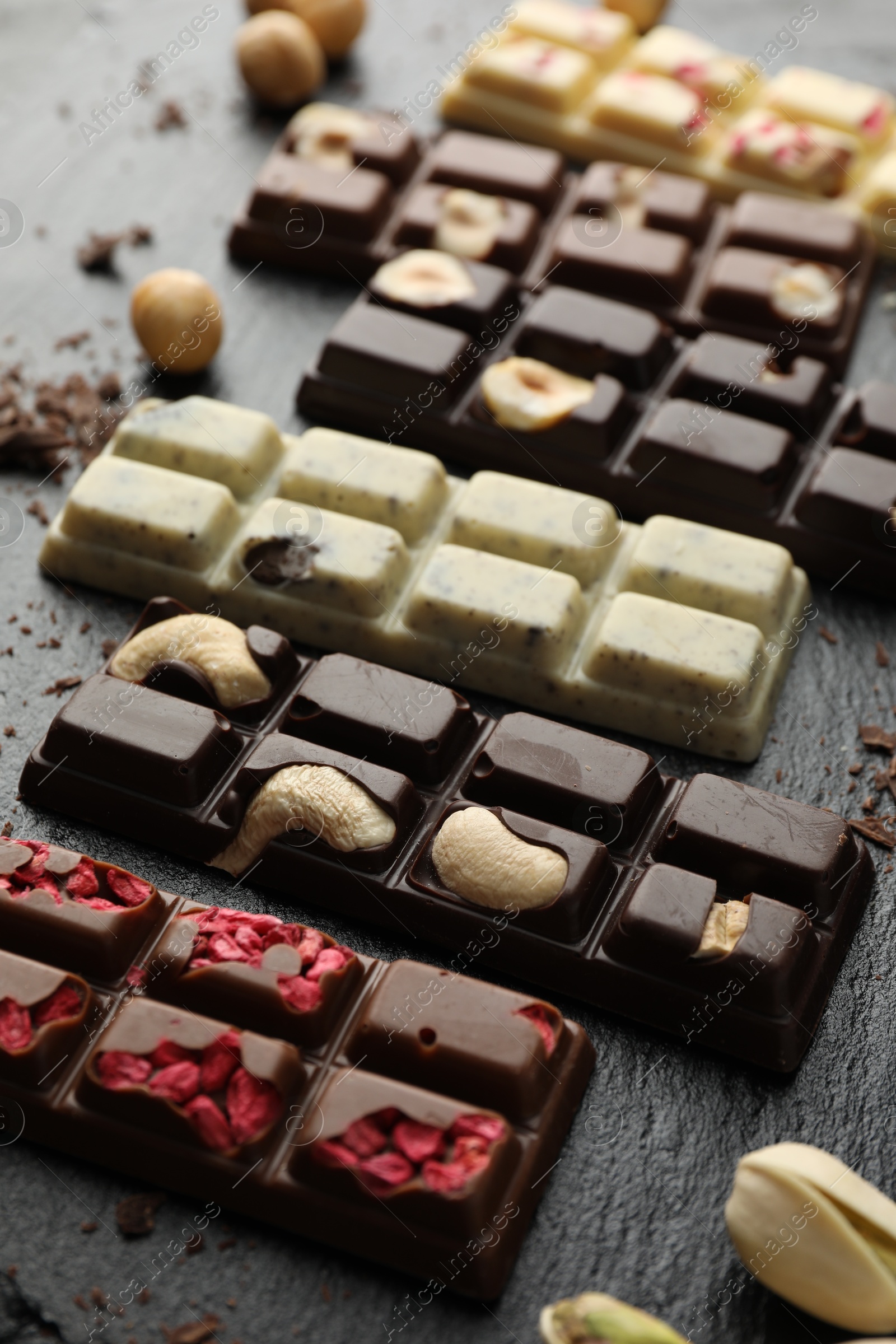 Photo of Different tasty chocolate bars with nuts and freeze dried raspberry on black table, closeup