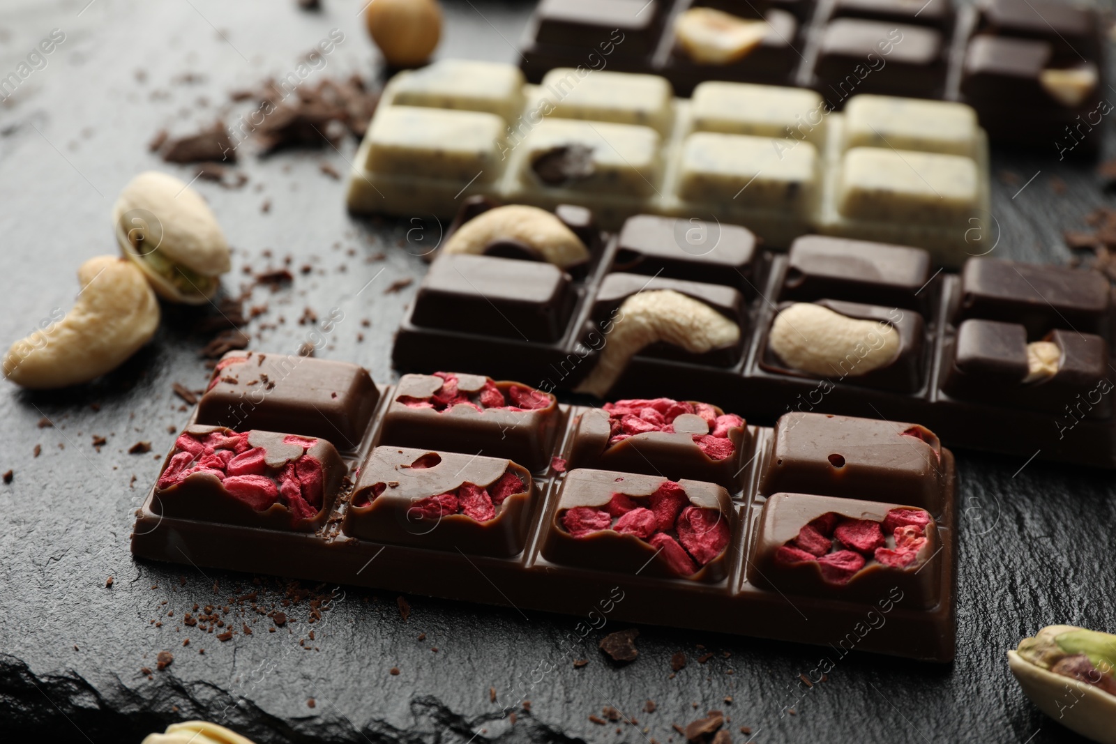 Photo of Different tasty chocolate bars with nuts and freeze dried raspberry on black table, closeup