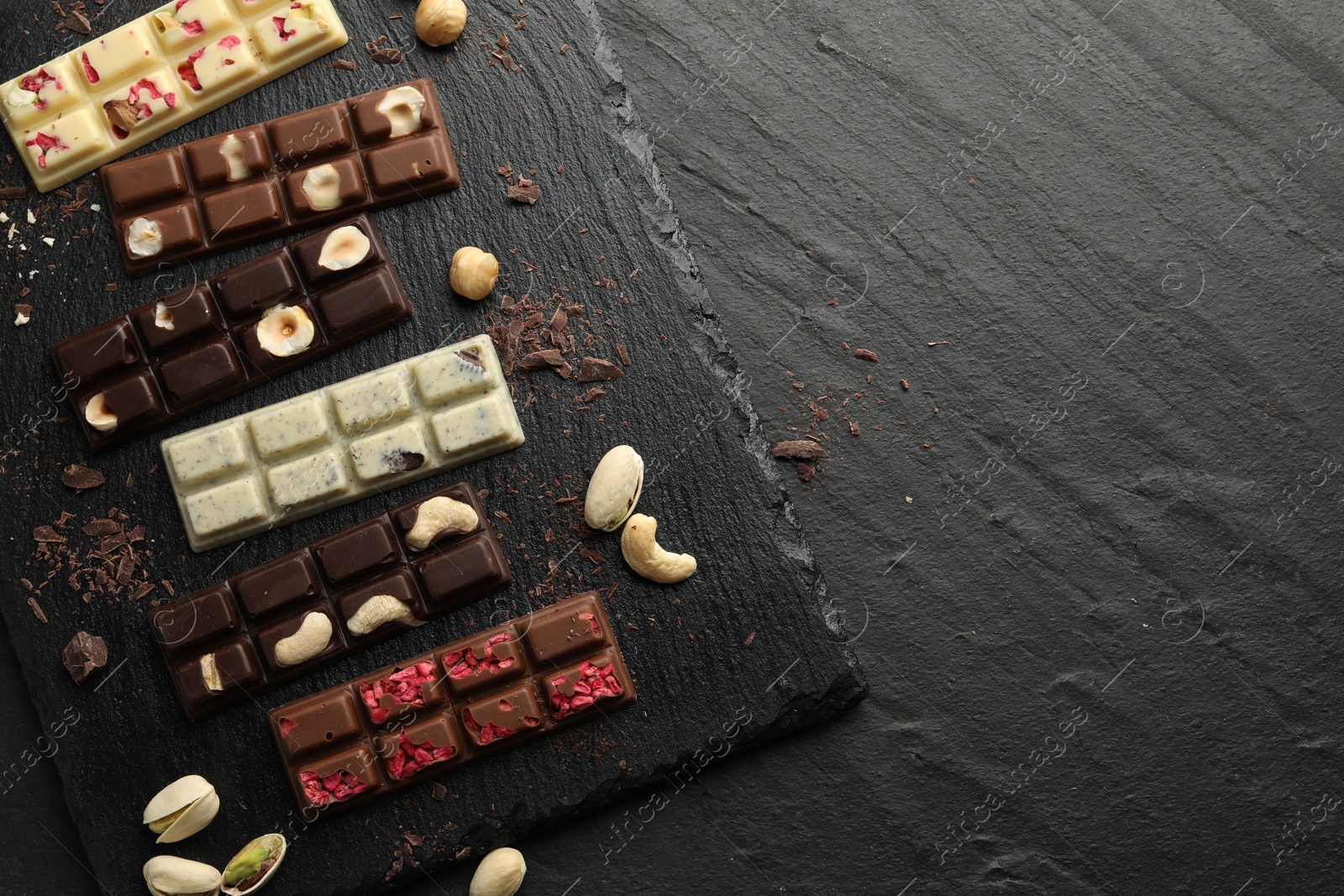 Photo of Different tasty chocolate bars with nuts and freeze dried raspberry on black table, flat lay. Space for text