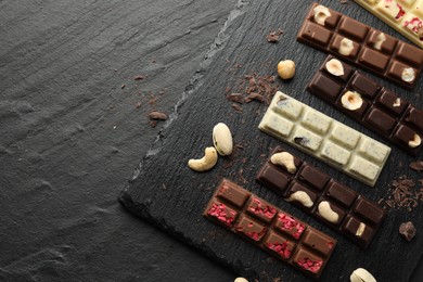 Photo of Different tasty chocolate bars with nuts and freeze dried raspberry on black table, flat lay. Space for text