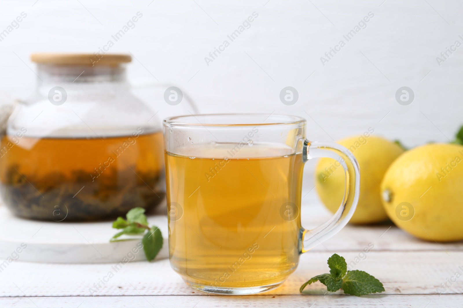 Photo of Aromatic mint tea with lemons and fresh leaves on white wooden table, closeup