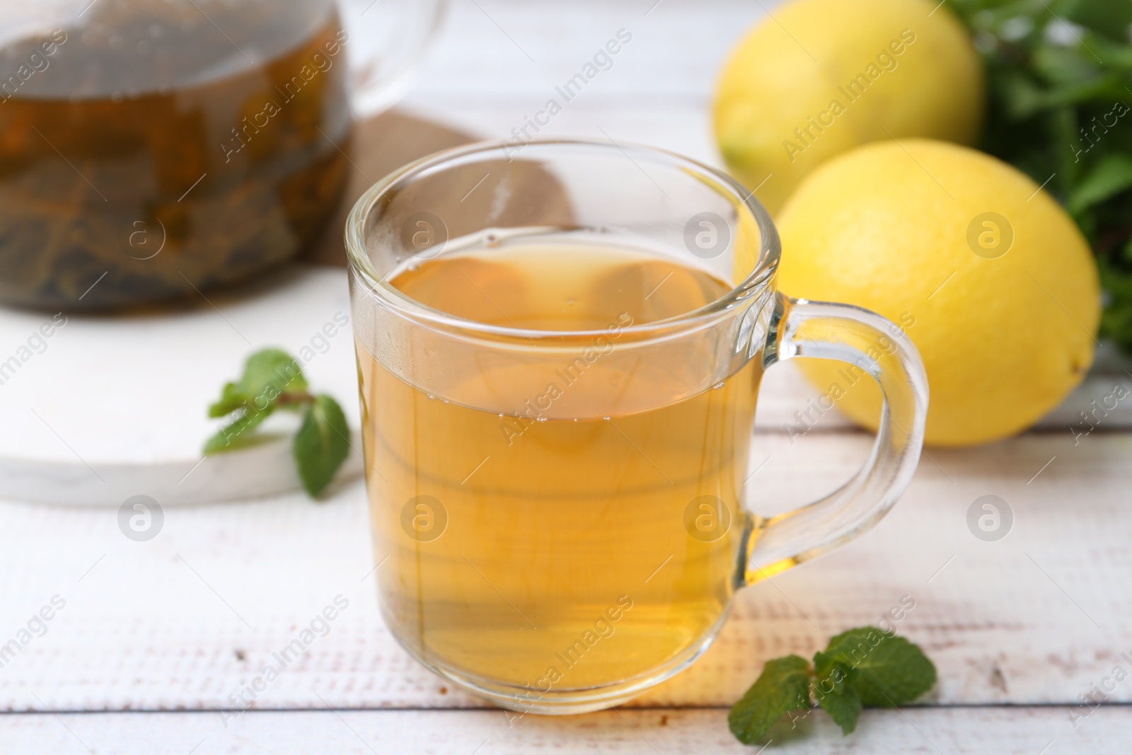 Photo of Aromatic mint tea with lemons and fresh leaves on white wooden table, closeup