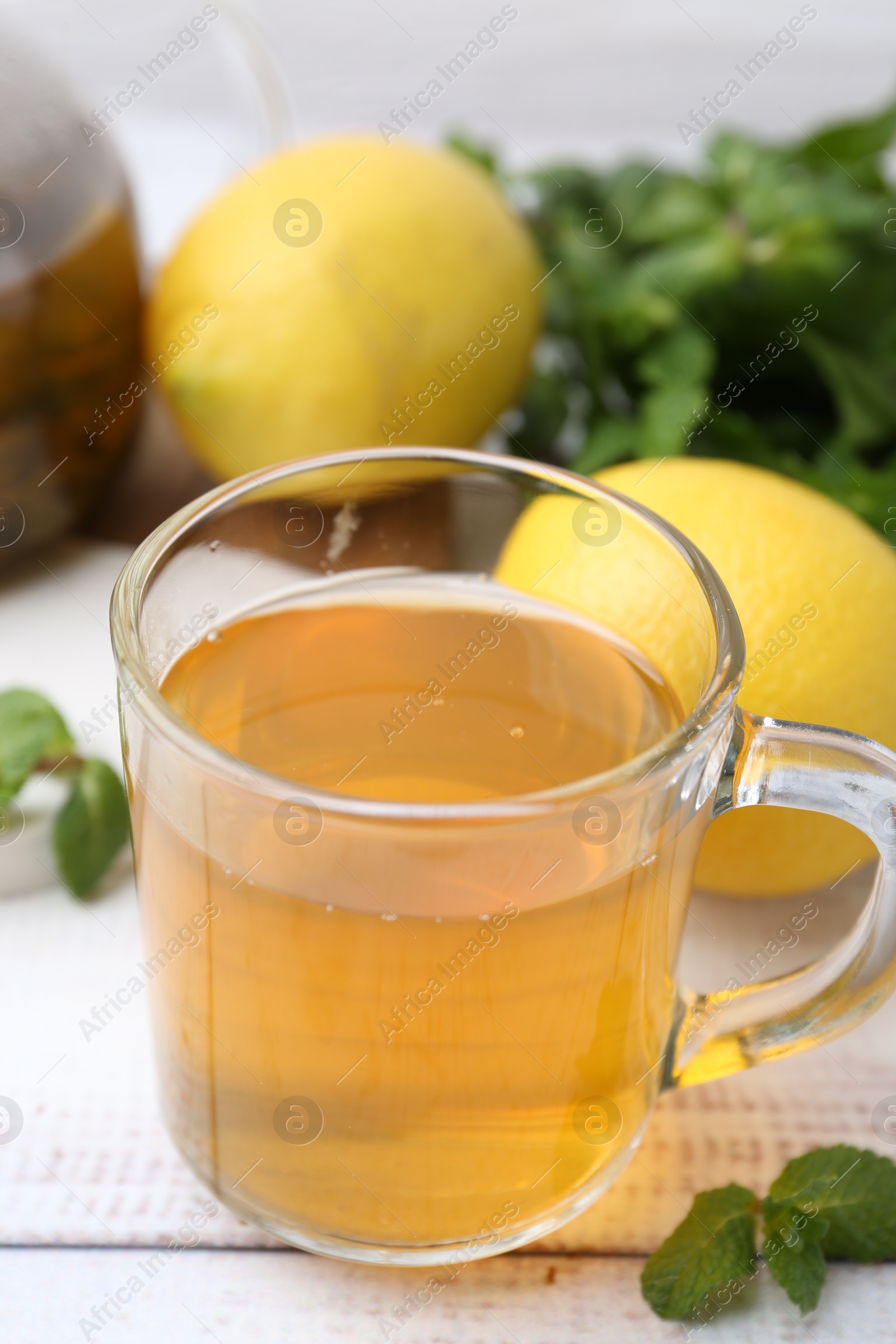 Photo of Aromatic mint tea with lemons and fresh leaves on white wooden table, closeup