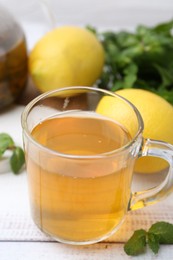 Photo of Aromatic mint tea with lemons and fresh leaves on white wooden table, closeup