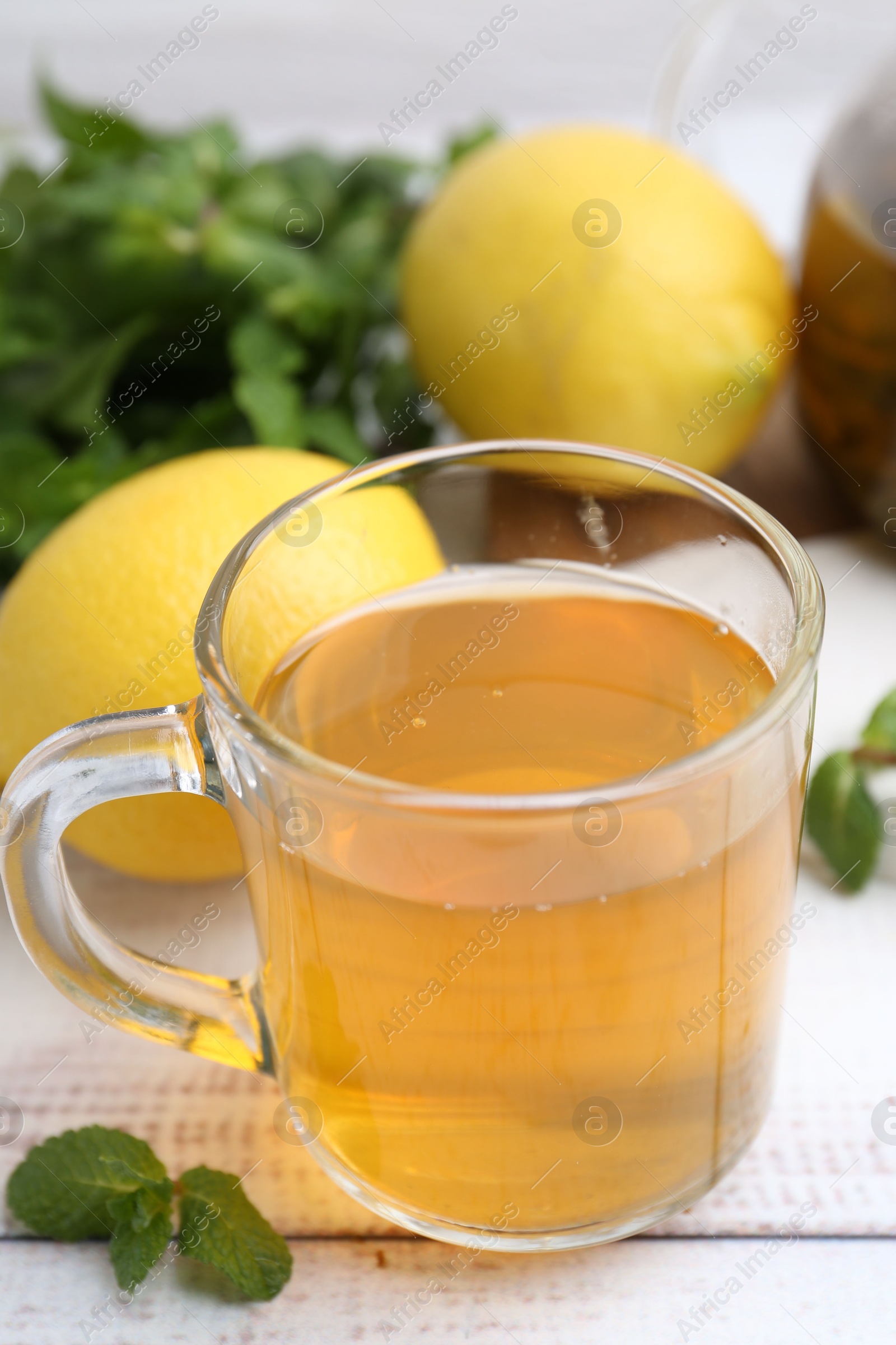 Photo of Aromatic mint tea with lemons and fresh leaves on white wooden table, closeup