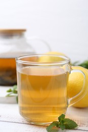 Photo of Aromatic mint tea with lemons and fresh leaves on white wooden table, closeup