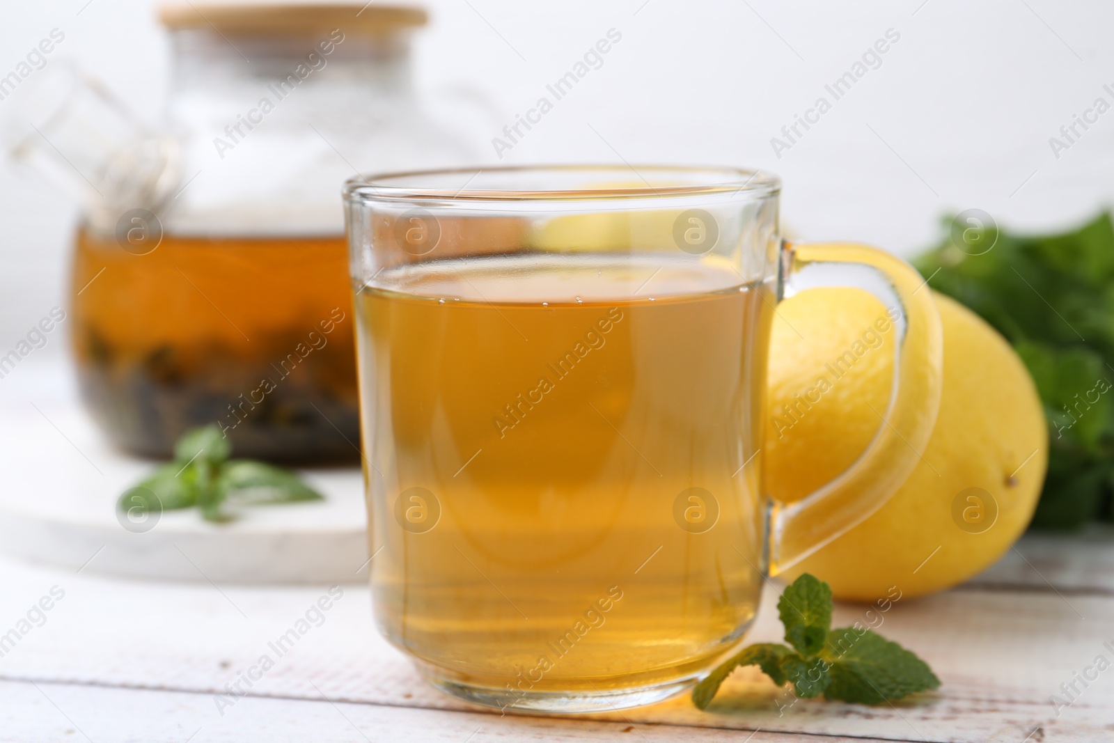 Photo of Aromatic mint tea with lemons and fresh leaves on white wooden table, closeup