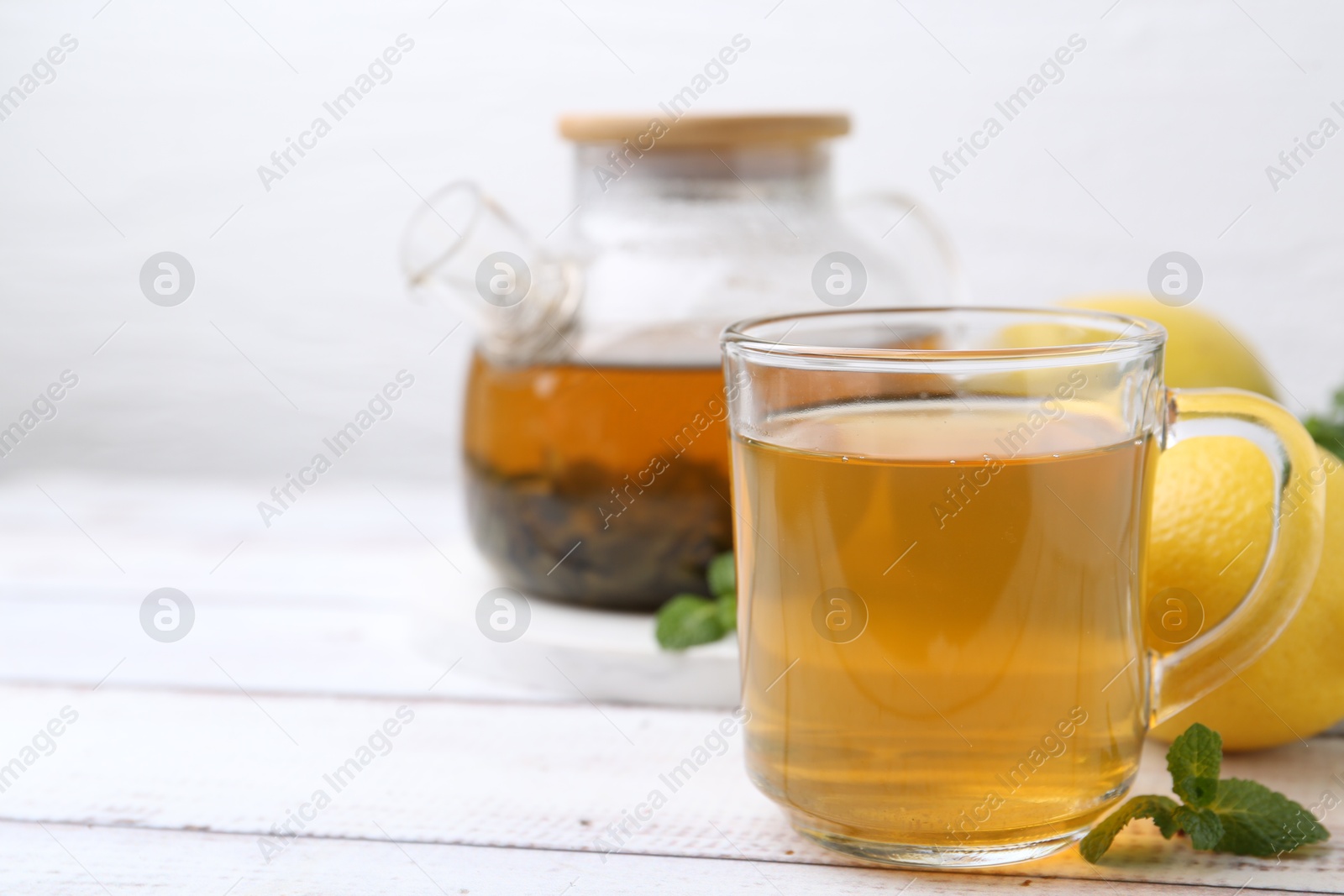 Photo of Aromatic mint tea with lemons and fresh leaves on white wooden table, closeup. Space for text