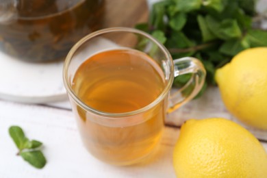 Photo of Aromatic mint tea with lemons and fresh leaves on white wooden table, closeup