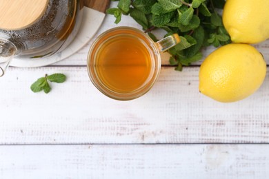 Photo of Aromatic mint tea with lemons and fresh leaves on white wooden table, flat lay. Space for text