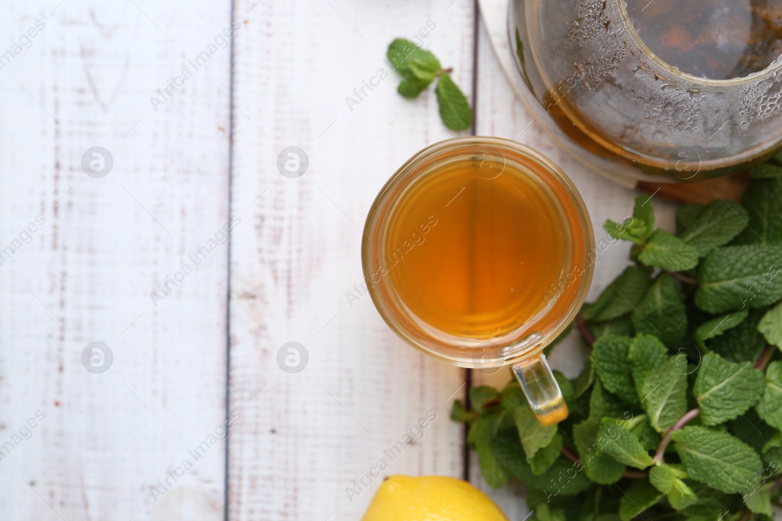 Photo of Aromatic mint tea and fresh leaves on white wooden table, flat lay. Space for text