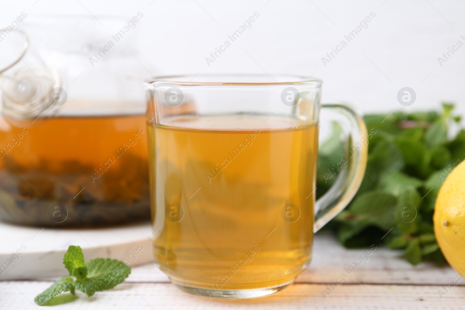 Photo of Aromatic mint tea and fresh leaves on white wooden table, closeup