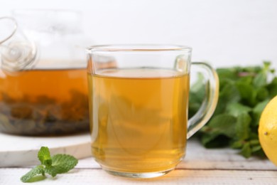 Photo of Aromatic mint tea and fresh leaves on white wooden table, closeup