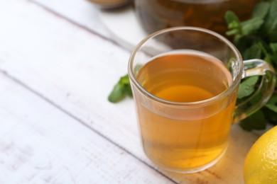 Photo of Aromatic mint tea and fresh leaves on white wooden table, closeup. Space for text