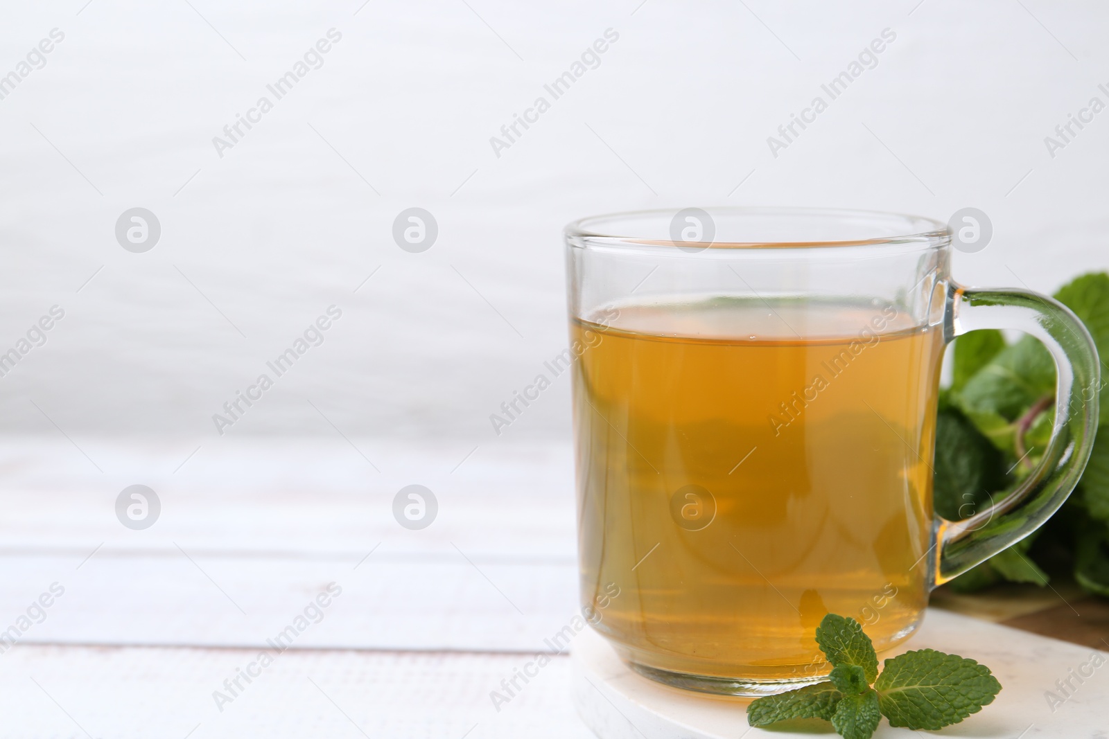 Photo of Aromatic mint tea and fresh leaves on white wooden table, closeup. Space for text