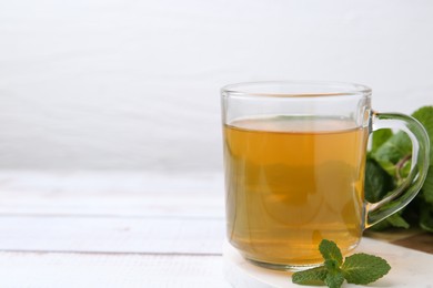 Photo of Aromatic mint tea and fresh leaves on white wooden table, closeup. Space for text