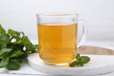 Photo of Aromatic mint tea and fresh leaves on white wooden table, closeup