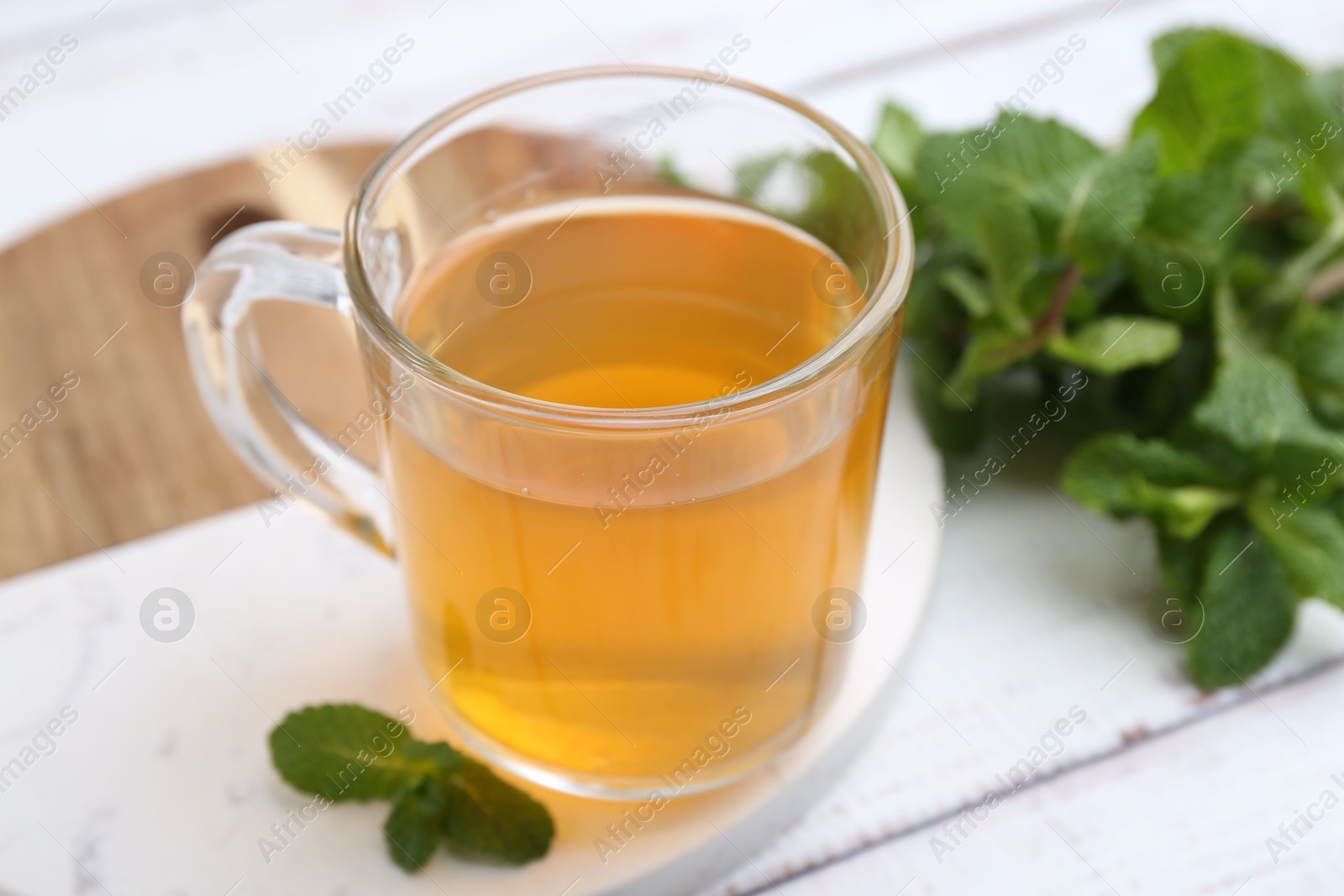 Photo of Aromatic mint tea and fresh leaves on white wooden table, closeup