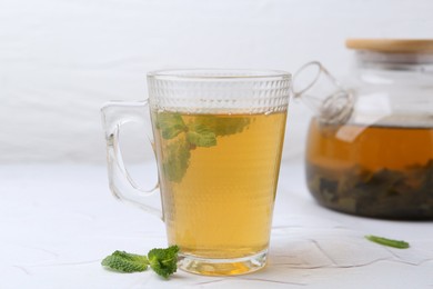 Photo of Aromatic mint tea and fresh leaves on white textured table, closeup