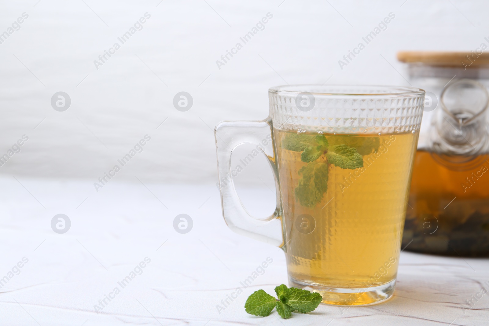 Photo of Aromatic mint tea and fresh leaves on white textured table, closeup. Space for text