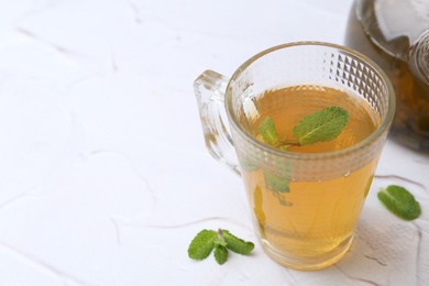 Photo of Aromatic mint tea and fresh leaves on white textured table, closeup. Space for text