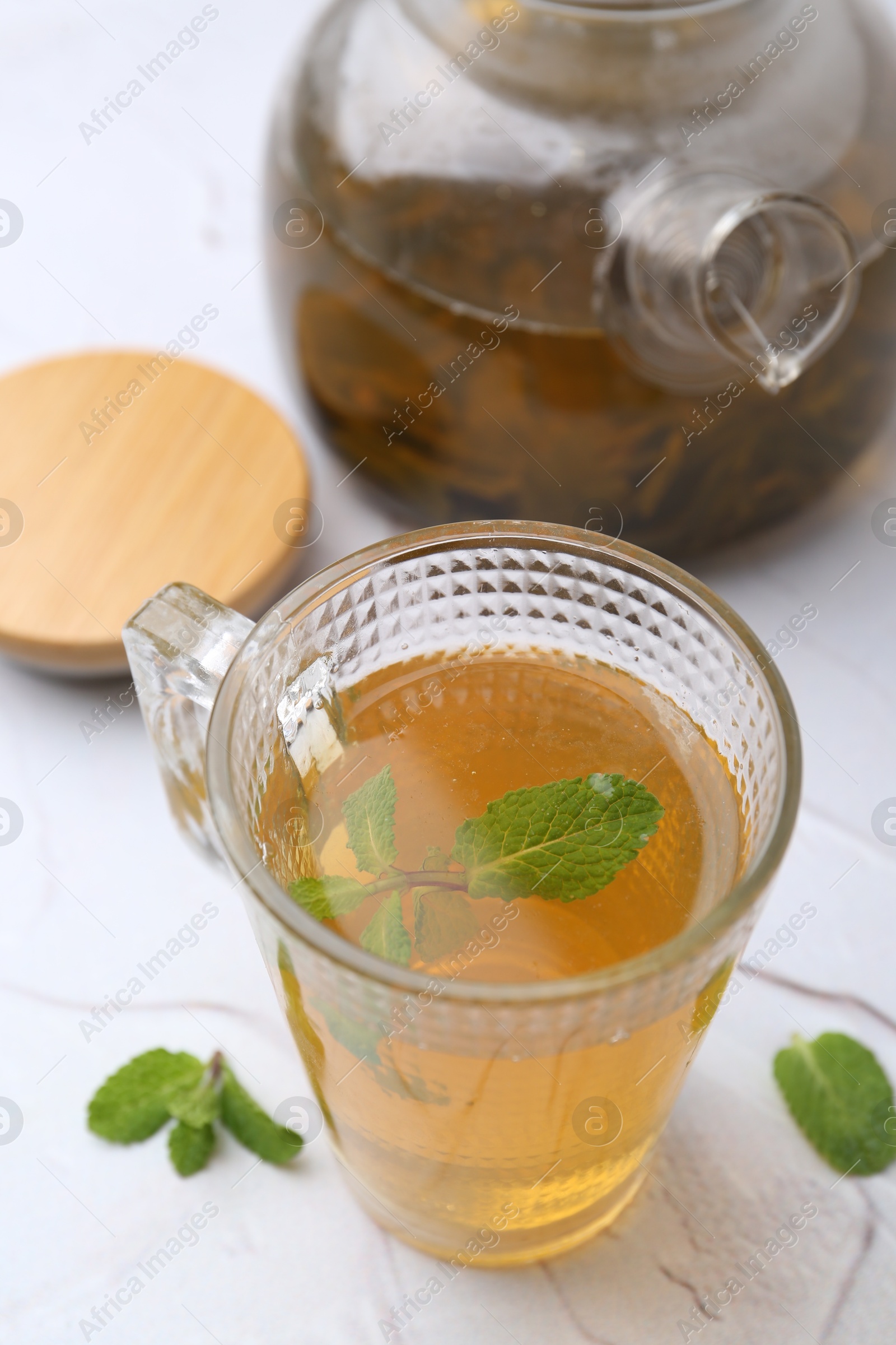 Photo of Aromatic mint tea and fresh leaves on white textured table, closeup