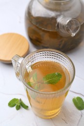 Photo of Aromatic mint tea and fresh leaves on white textured table, closeup