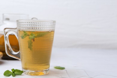 Photo of Aromatic mint tea and fresh leaves on white textured table, closeup. Space for text