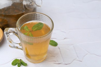 Photo of Aromatic mint tea and fresh leaves on white textured table, closeup. Space for text