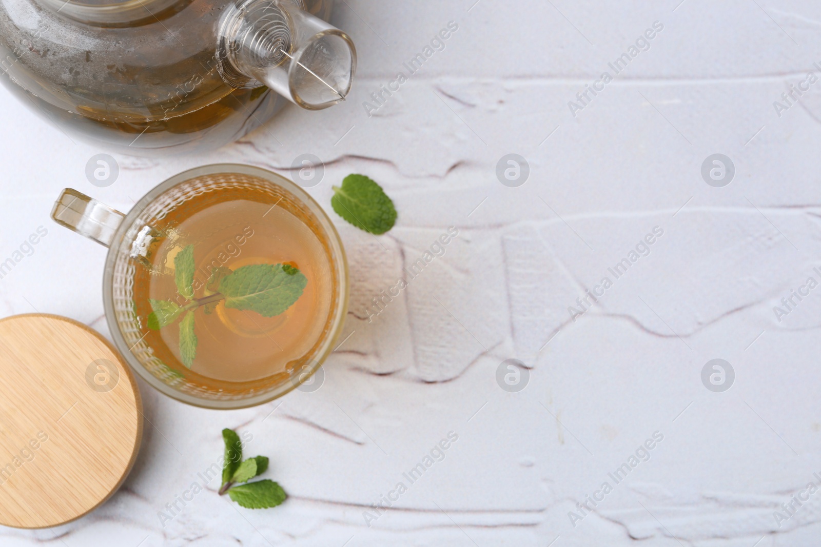 Photo of Aromatic mint tea and fresh leaves on white textured table, flat lay. Space for text