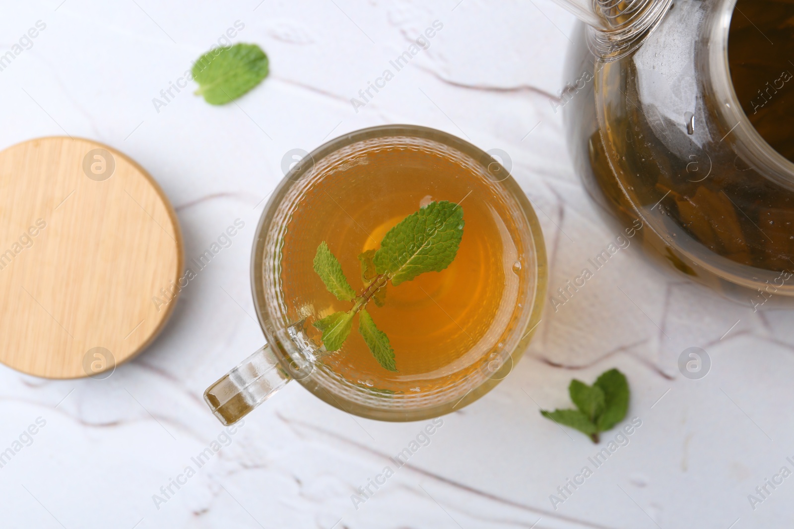 Photo of Aromatic mint tea and fresh leaves on white textured table, flat lay