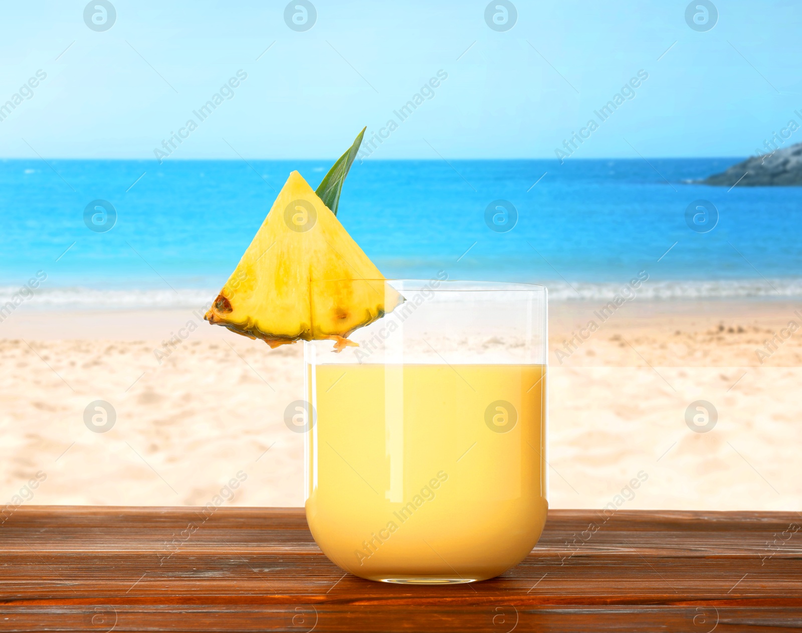 Image of Tasty pineapple cocktail or smoothie in glass on wooden table against seascape